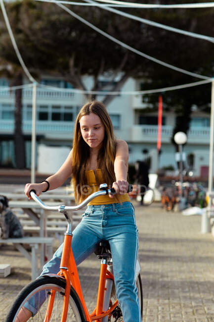 Front view of a Caucasian girl with long hair enjoying time hanging out on a sunny day, riding a bike in a urban pedestrian area. — Stock Photo