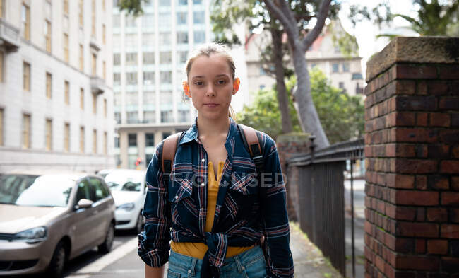 Портрет белой девушки в клетчатой рубашке, наслаждающейся жизнью в солнечный день, стоящей на тротуаре, смотрящей прямо в камеру. — стоковое фото
