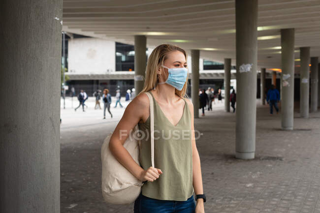 Vue latérale d'une femme caucasienne dans les rues de la ville pendant la journée, portant un masque facial contre la pollution atmosphérique et le coronavirus covid19. — Photo de stock