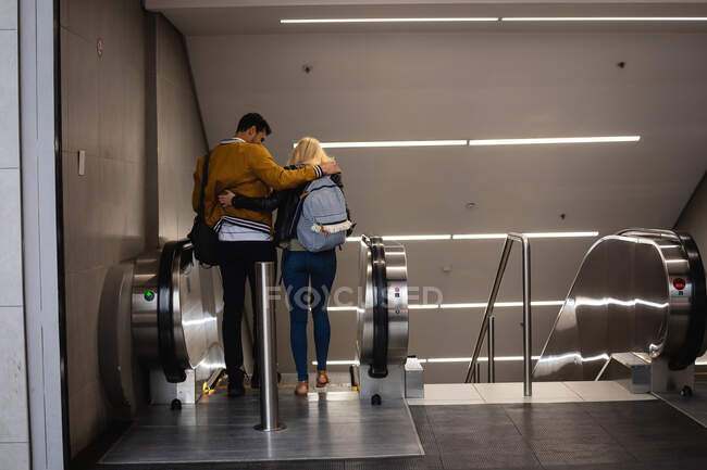 Visão traseira de um casal caucasiano na cidade, descendo em uma estação de metrô em uma escada rolante . — Fotografia de Stock