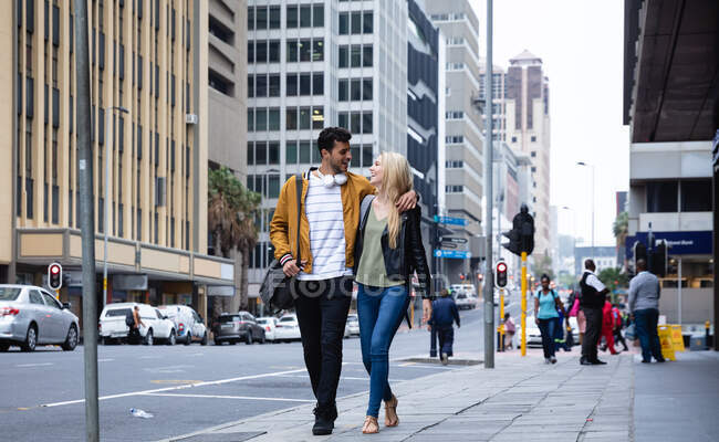 Vista frontale di una felice coppia caucasica in giro per le strade della città durante il giorno, abbracciando e sorridendo. — Foto stock