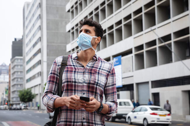 Nahaufnahme eines kaukasischen Mannes mit kariertem Hemd und Gesichtsmaske gegen Luftverschmutzung und Covid19 Coronavirus, der mit seinem Smartphone durch die Straßen der Stadt läuft. — Stockfoto