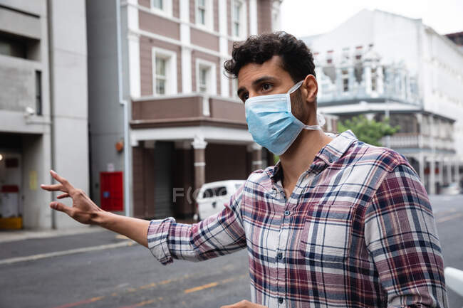 Vista frontal de cerca de un hombre caucásico con camisa a cuadros y máscara facial contra la contaminación del aire y covid19 coronavirus, llamando a un taxi en la calle. - foto de stock