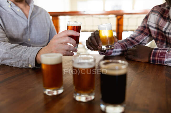 Männer in der Mitte probieren Bier und stoßen auf eine Mikrobrauerei-Kneipe an. — Stockfoto