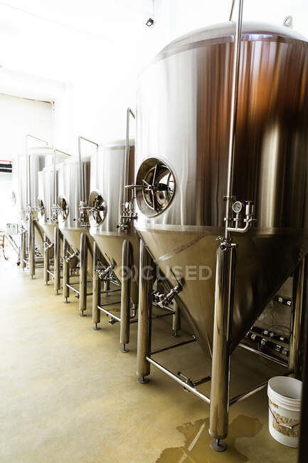 Vista de cerca de cinco cubas de plata colocadas a lo largo de la pared en un pequeño compartimento de fermentación cervecera con paredes pintadas de blanco. - foto de stock
