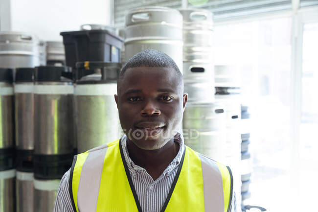 Portrait of an African American man working in a microbrewery, wearing high visibility vest and looking straight into a camera. — Stock Photo