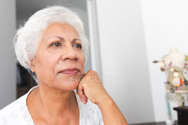 Крупным планом привлекательной пожилой афроамериканки на пенсии дома в ее спальне, отводя взгляд и думая, самоизоляция во время пандемии коронавируса — стоковое фото