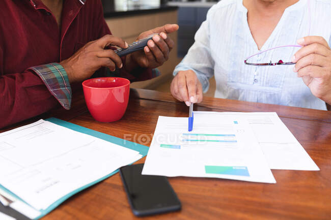 Mid section of a senior retired African American couple sitting at a table in their dining room drinking coffee, looking at paperwork and discussing their finances, at home together isolating during coronavirus covid19 pandemic — Stock Photo