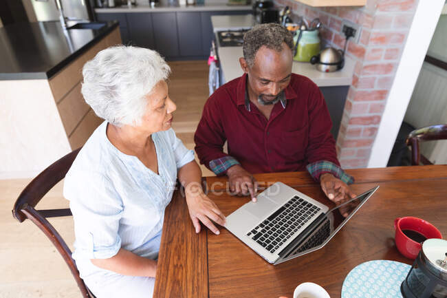 Vue en angle élevé d'un couple afro-américain retraité âgé assis à une table dans sa salle à manger, utilisant un ordinateur portable ensemble, à la maison isolant ensemble pendant une pandémie de coronavirus covid19 — Photo de stock