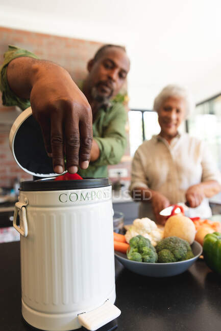 Glückliche ältere afroamerikanische Rentnerehepaar zu Hause, Essen zubereiten, Gemüse schneiden, den Abfall in einen Kompostbehälter in ihrer Küche, zu Hause zusammen isolieren während Coronavirus covid19 Pandemie — Stockfoto