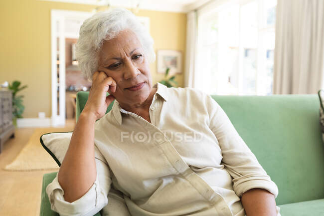 Großaufnahme einer glücklichen älteren afroamerikanischen Rentnerin zu Hause, die in ihrem Wohnzimmer sitzt, sich auf ihre Hand stützt und denkt, sich während der Coronavirus-Pandemie selbst isoliert 19 — Stockfoto