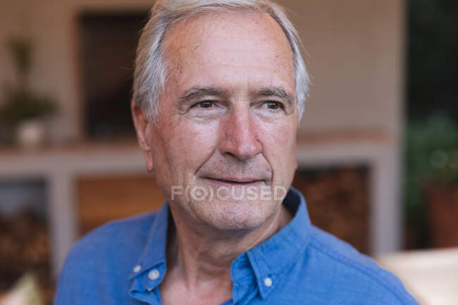 Retrato de cerca de un hombre caucásico mayor guapo disfrutando de su retiro, en casa, mirando hacia otro lado y sonriendo, auto aislado durante la pandemia del coronavirus covid19 - foto de stock