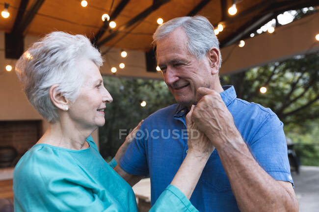 Feliz pareja de ancianos caucásicos jubilados en casa tomados de la mano, bailando juntos y sonriendo, en casa juntos aislando durante coronavirus covid19 pandemia - foto de stock