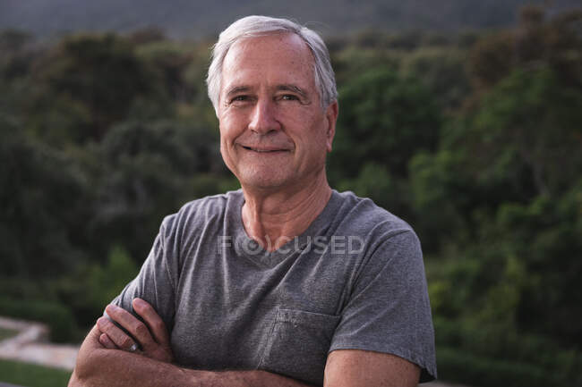 Portrait of a handsome senior Caucasian man enjoying his retirement, in a garden in the sun looking to camera smiling with arms crossed, self isolating during coronavirus covid19 pandemic — Stock Photo