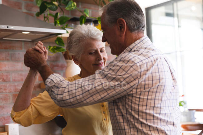 Close up of happy retired senior Caucasian couple at home holding hands, dancing together in their kitchen and smiling, at home together isolating during coronavirus covid19 pandemic — Stock Photo