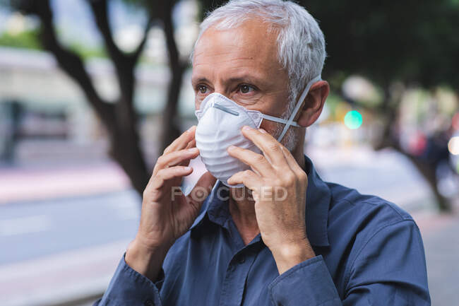 Hombre caucásico mayor fuera y alrededor de las calles de la ciudad durante el día, con una máscara facial contra el coronavirus, covid 19.Ponerse la máscara facial contra la contaminación del aire y el coronavirus. - foto de stock
