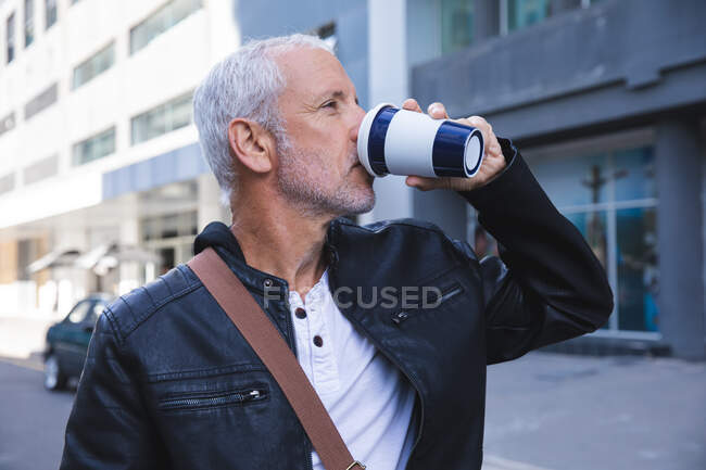 Uomo anziano caucasico, indossa abiti casual, in giro per le strade della città durante il giorno, bevendo caffè da asporto.. — Foto stock