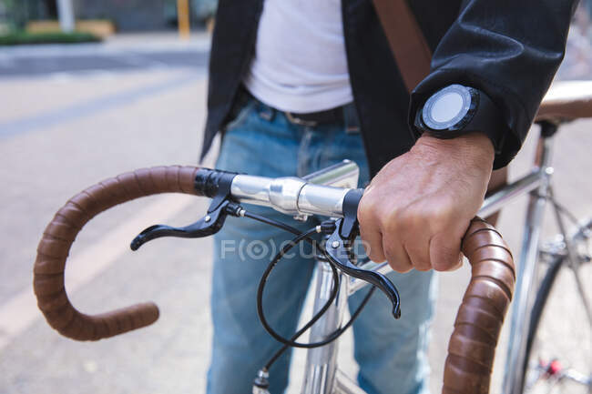 Mid section of man, wearing smartwatch, out and about in the city streets during the day, wheeling a bicycle. — Stock Photo