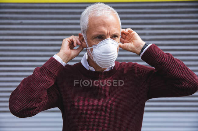 Homem caucasiano sênior para fora e sobre nas ruas da cidade durante o dia, colocando uma máscara facial contra coronavírus, covid 19 . — Fotografia de Stock