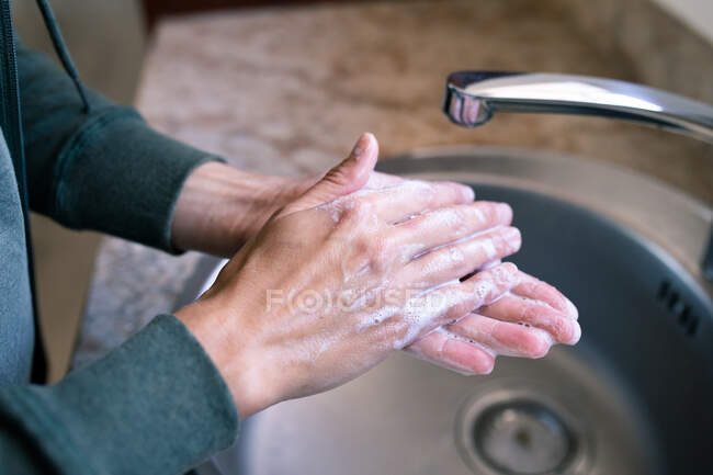 Primer plano de la mujer en casa en el baño durante el día lavándose las manos en un fregadero, usando jabón, protección contra la infección por coronavirus Covid-19 y pandemia. Distanciamiento social y autoaislamiento en cuarentena - foto de stock
