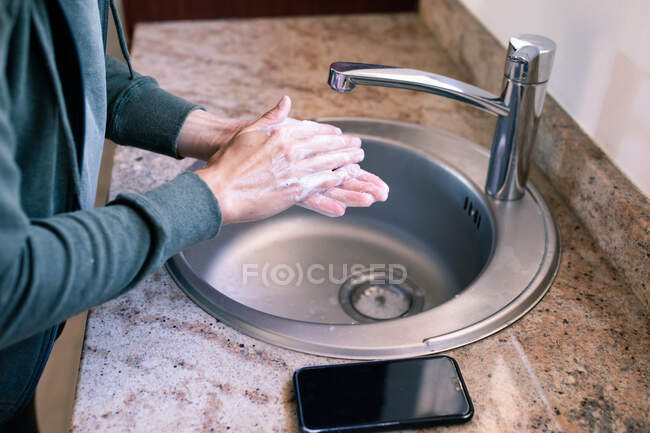 Primer plano de la mujer en casa en el baño durante el día lavándose las manos en un fregadero, usando jabón, protección contra la infección por coronavirus Covid-19 y pandemia. Distanciamiento social y autoaislamiento en cuarentena - foto de stock