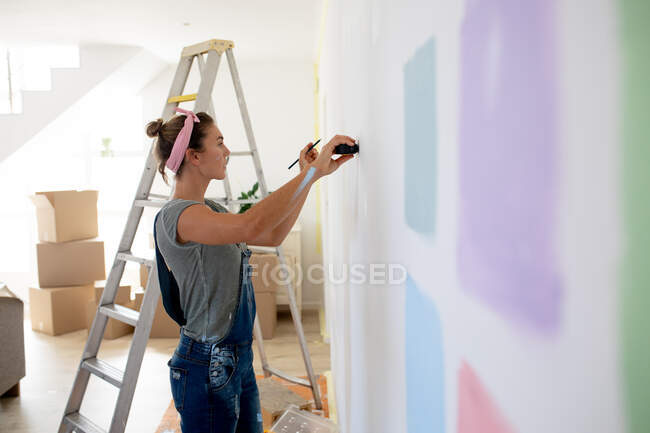 Caucasian woman wearing blue jeans dungarees, spending time at home self isolating and social distancing in quarantine lockdown during coronavirus covid 19 epidemic, renovating her home. — Stock Photo