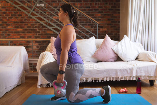 Mulher branca vlogger em casa em sua sala de estar, demonstrando exercícios com sinos de despejo para seu blog online. Distanciamento social e auto-isolamento em quarentena . — Fotografia de Stock