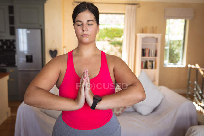 Vlogger mujer caucásica en casa en su sala de estar, demostrando ejercicio de yoga para su blog en línea. Distanciamiento social y autoaislamiento en cuarentena. - foto de stock