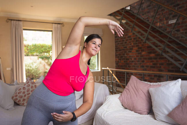 Кавказская женщина-блогер дома, в своей гостиной, демонстрирует упражнения на растяжку для своего онлайн-блога. Социальное дистанцирование и самоизоляция в карантинной изоляции. — стоковое фото