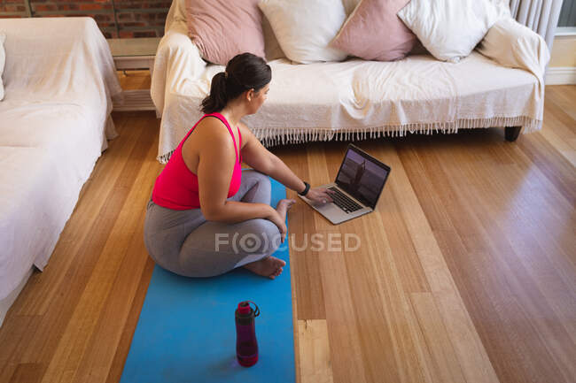 Caucasian female vlogger at home in her sitting room, exercising and using her laptop computer. Social distancing and self isolation in quarantine lockdown. — Stock Photo