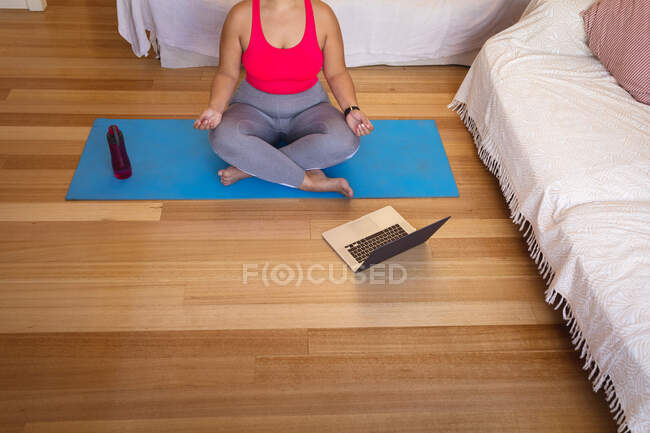 Низкая часть женщины-блогера дома в гостиной, практикует йогу и использует свой ноутбук. Социальное дистанцирование и самоизоляция в карантинной изоляции. — стоковое фото