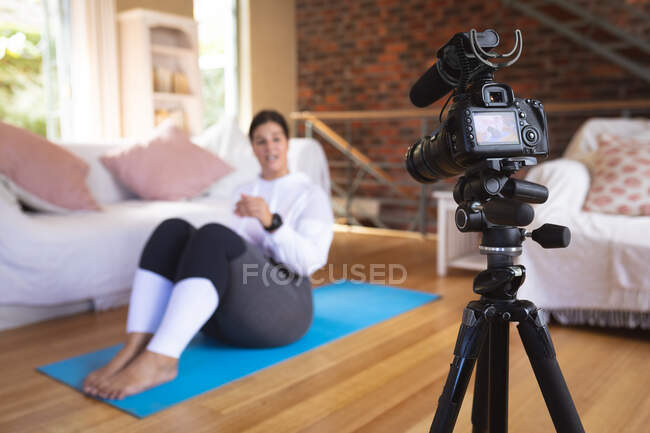 Vlogger mujer caucásica en casa en su sala de estar, demostrando ejercicios para su grabación de blog en línea con una cámara. Distanciamiento social y autoaislamiento en cuarentena. - foto de stock