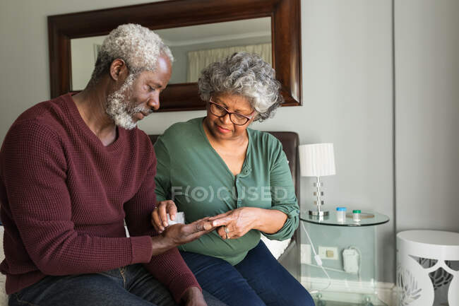 A senior African American couple spending time at home together, social distancing and self isolation in quarantine lockdown during coronavirus covid 19 epidemic, the woman pouring tablets from a bottle into hand of the man — Stock Photo
