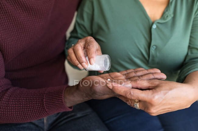 Mid section of African American couple spending time at home together, social distancing and self isolation in quarantine lockdown during coronavirus covid 19 epidemic, the woman pouring tablets from a bottle into hand of the man — Stock Photo