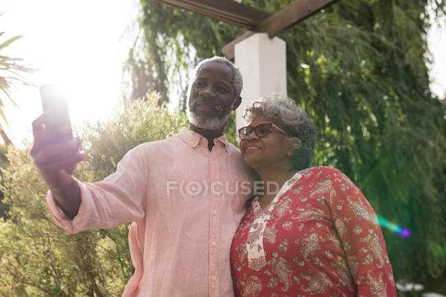 Ein älteres afroamerikanisches Paar verbringt während der Coronavirus-Epidemie 19 Zeit in seinem Garten, soziale Distanzierung und Selbstisolierung in Quarantäne, der Mann hält ein Smartphone in der Hand und macht ein Selfie — Stockfoto