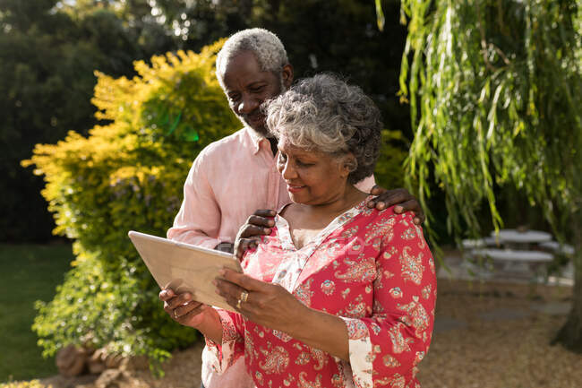 Una coppia di afroamericani anziani che trascorrono del tempo insieme nel loro giardino, distanziamento sociale e isolamento in quarantena durante l'epidemia di coronavirus covid 19, usando un tablet — Foto stock