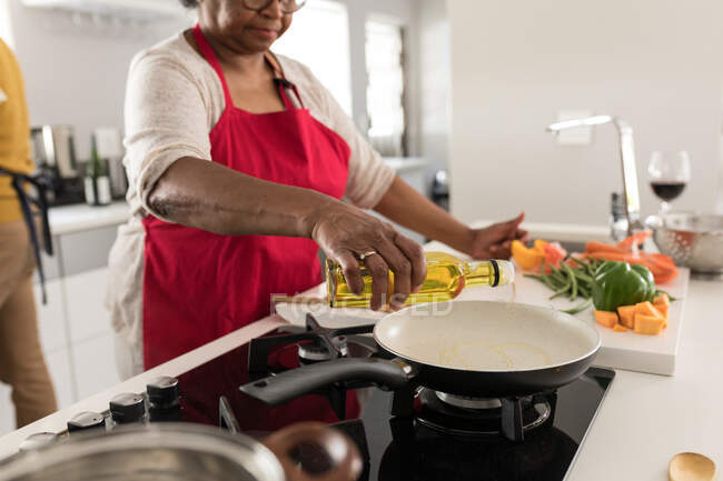 Старша афроамериканська пара проводить час вдома разом, спілкуючись і самоізолюючись під час карантину під час епідемії коронавірусу (19), стоячи на кухні, готуючи їжу. — стокове фото