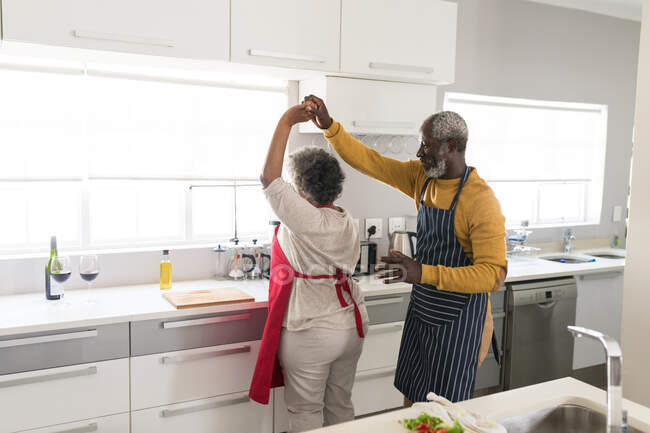 Старша афроамериканська пара проводить час вдома разом, спілкуючись і самоізолюючись під час карантину під час епідемії коронавірусу (19), танцюючи на кухні. — стокове фото