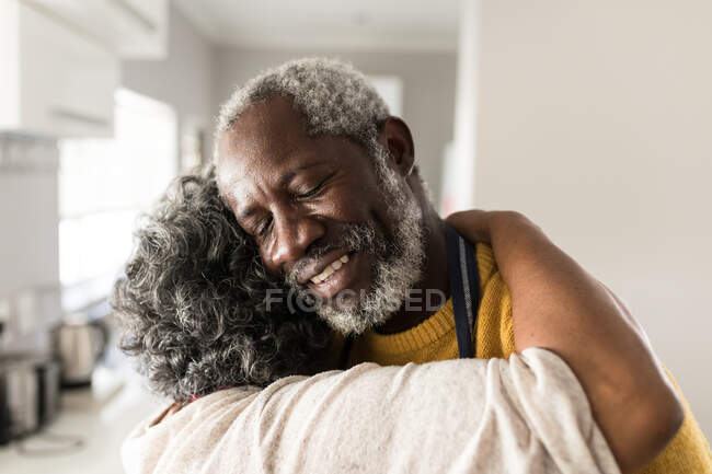 Старша афроамериканська пара проводить час вдома разом, спілкуючись і самоізолюючись під час карантинної блокади під час коронавірусу (19 епідемії), обіймаючи, посміхаючись. — стокове фото