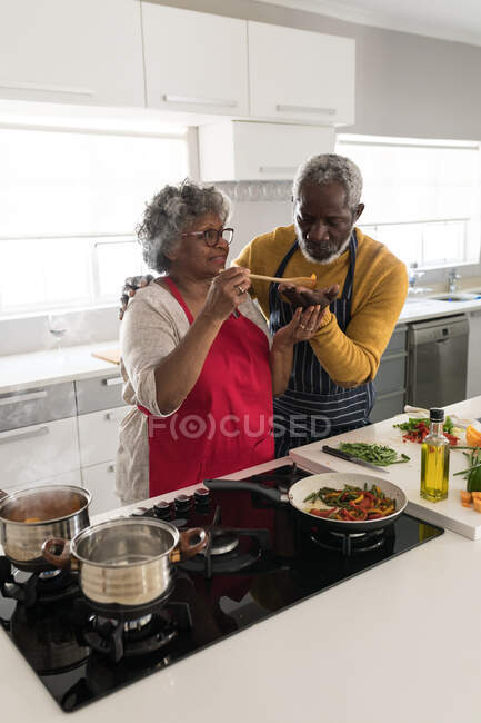 Um casal afro-americano sênior passando tempo em casa juntos, distanciamento social e auto-isolamento em quarentena durante coronavírus covid 19 epidemia, de pé na cozinha preparando alimentos — Fotografia de Stock