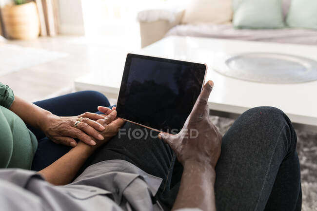 Средняя часть афроамериканской пары проводит время дома вместе, социальное дистанцирование и самоизоляция в карантинной изоляции во время эпидемии коронавируса ковида 19, используя таблетку — стоковое фото