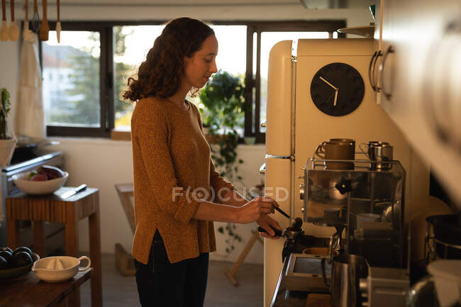 Kaukasische Frau, die während der 19-jährigen Coronavirus-Epidemie selbstisolierend und sozial distanziert in Quarantäne lebt, steht in ihrer Küche und bereitet Kaffee zu. — Stockfoto