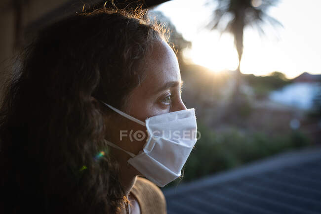 Caucasian woman spending time at home self isolating and social distancing in quarantine lockdown during coronavirus covid 19 epidemic, wearing a face mask against covid19 coronavirus, sitting by a window. — Stock Photo