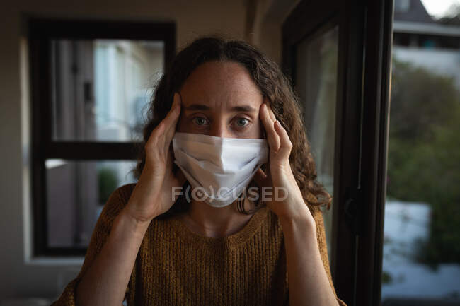 Portrait of a Caucasian woman spending time at home self isolating, wearing a face mask against covid19 coronavirus, looking straight into a camera. — Stock Photo