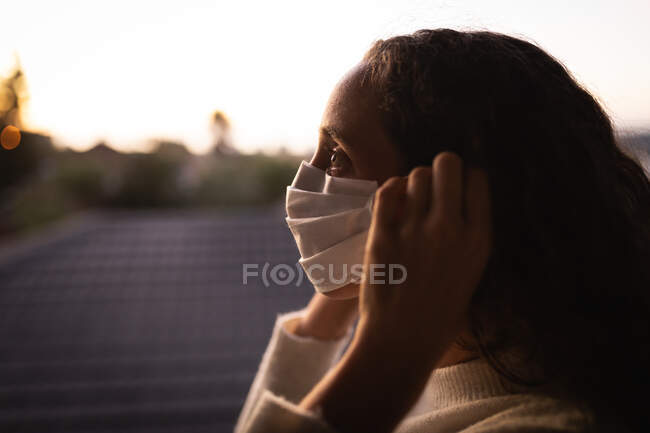 Femme caucasienne passant du temps à la maison à s'isoler et à prendre ses distances sociales en quarantaine pendant l'épidémie de coronavirus covide 19, portant un masque facial contre le coronavirus covid19, debout près d'une fenêtre. — Photo de stock