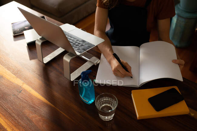Blick von oben auf die Frau, die Zeit zu Hause verbringt, am Schreibtisch sitzt und arbeitet, ihren Laptop und ihr Notebook benutzt. Soziale Distanzierung und Selbstisolierung in Quarantäne. — Stockfoto