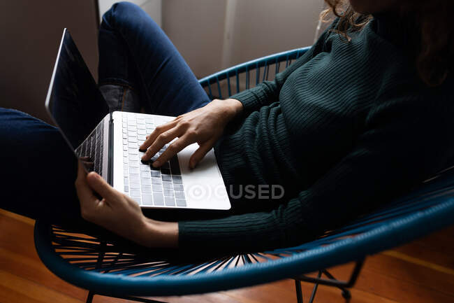Parte média da mulher passando tempo em casa, sentada em uma cadeira e usando seu laptop. Distanciamento social e auto-isolamento em quarentena . — Fotografia de Stock