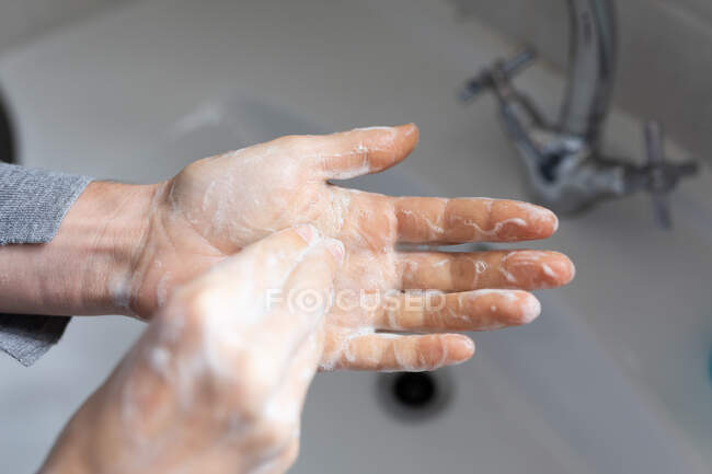 Cerca de la mitad de la sección de la mujer que usa suéter gris, lavándose las manos con jabón líquido. Distanciamiento social y autoaislamiento en cuarentena. - foto de stock