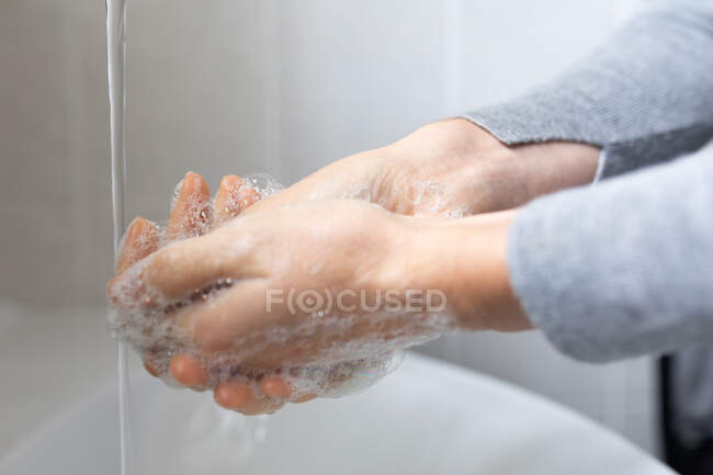 Cerca de la mitad de la sección de la mujer que usa suéter gris, lavándose las manos con jabón líquido. Distanciamiento social y autoaislamiento en cuarentena. - foto de stock