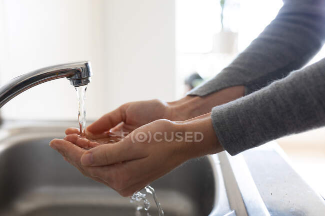 Fermer la section médiane de la femme portant un pull gris, se lavant les mains avec de l'eau courante. Distance sociale et isolement personnel en quarantaine. — Photo de stock